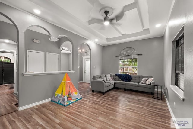 living room featuring a raised ceiling, ceiling fan, and wood-type flooring