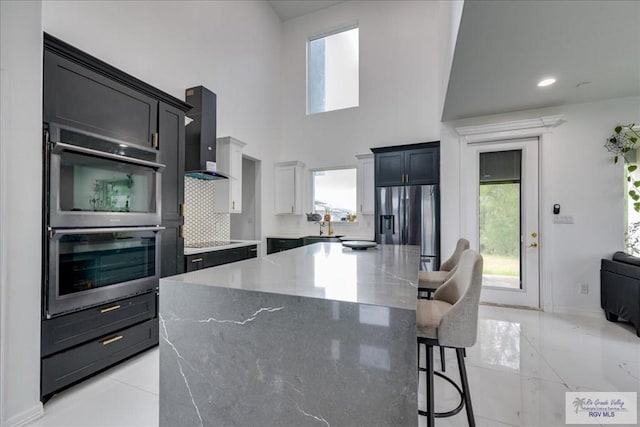 3213 E Westgate Cir, Harlingen, TX 78552 - kitchen featuring wall chimney exhaust hood, appliances with stainless steel finishes, a breakfast bar area, light stone counters, and a kitchen island
