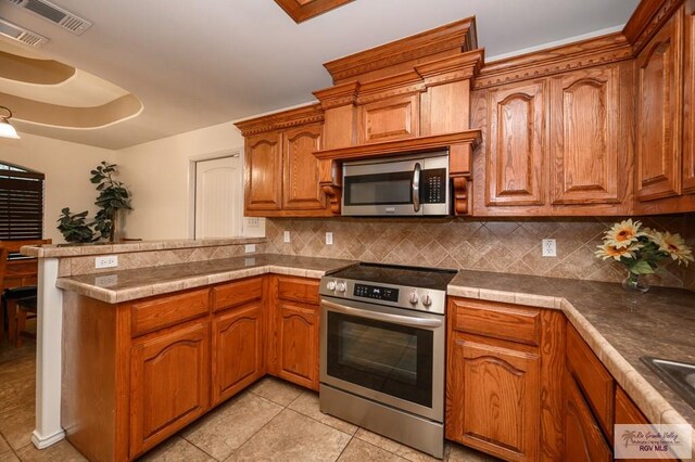 kitchen with backsplash, kitchen peninsula, light tile patterned floors, and stainless steel appliances