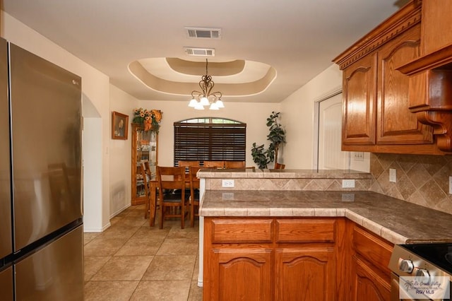 kitchen featuring backsplash, stainless steel appliances, a raised ceiling, decorative light fixtures, and an inviting chandelier