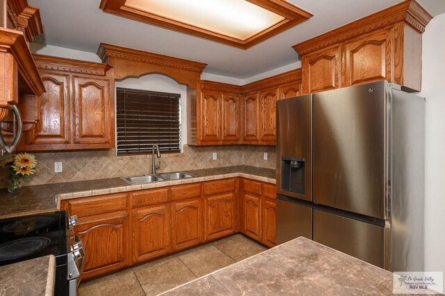 kitchen with sink, black electric range, backsplash, stainless steel fridge, and light tile patterned flooring