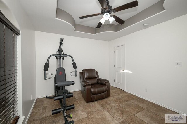 workout room featuring a raised ceiling and ceiling fan