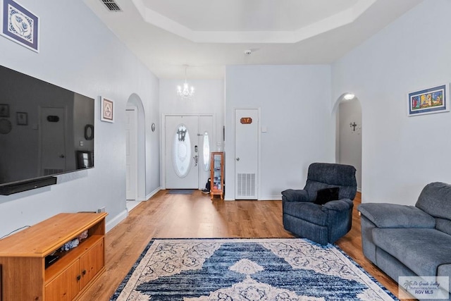 2518 Thomas Ln, Harlingen, TX 78550 - living room with arched walkways, light wood-type flooring, a chandelier, a tray ceiling, and baseboards