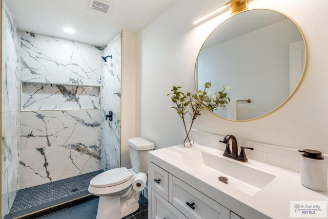 bathroom featuring vanity, toilet, and a tile shower