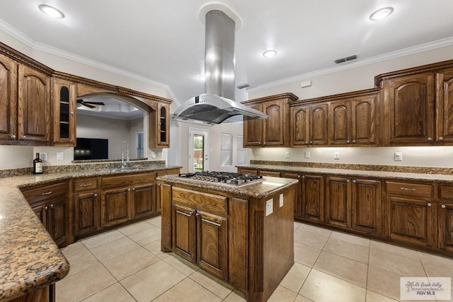 5302 Remington Dr, Harlingen, TX 78552 - kitchen with stainless steel gas cooktop, island exhaust hood, ornamental molding, glass insert cabinets, and a kitchen island