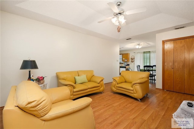 living room with a tray ceiling, visible vents, a ceiling fan, and light wood finished floors