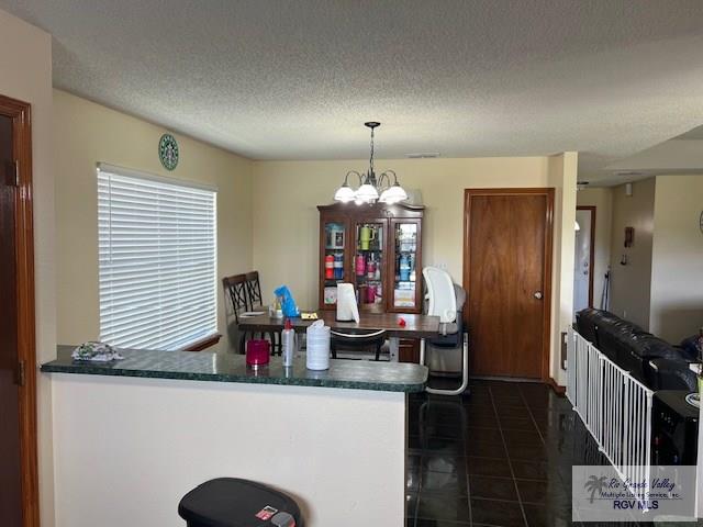 kitchen featuring dark tile patterned flooring, decorative light fixtures, a textured ceiling, a notable chandelier, and kitchen peninsula