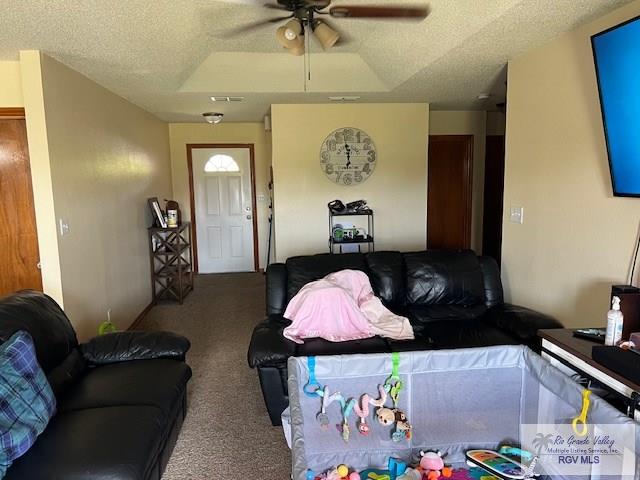 living room with a textured ceiling, carpet floors, a tray ceiling, and ceiling fan