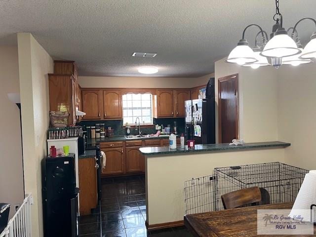 kitchen with sink, an inviting chandelier, dark tile patterned floors, decorative light fixtures, and black refrigerator