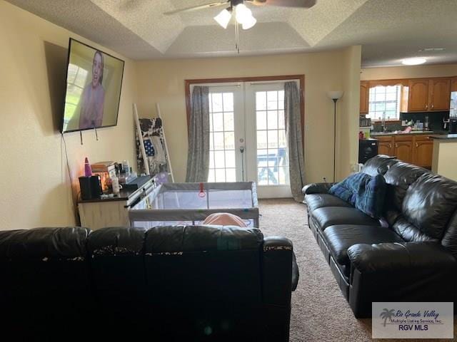 carpeted living room with french doors, a textured ceiling, a tray ceiling, ceiling fan, and sink