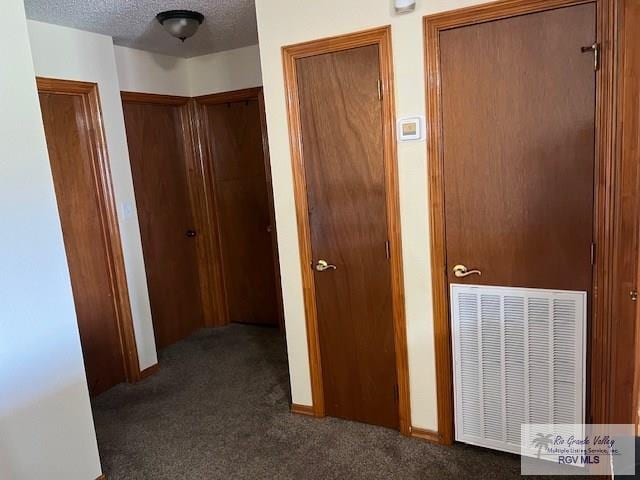 corridor with dark carpet and a textured ceiling