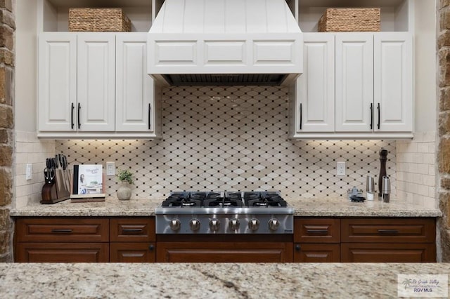 kitchen with tasteful backsplash, light stone counters, premium range hood, stainless steel gas stovetop, and white cabinets