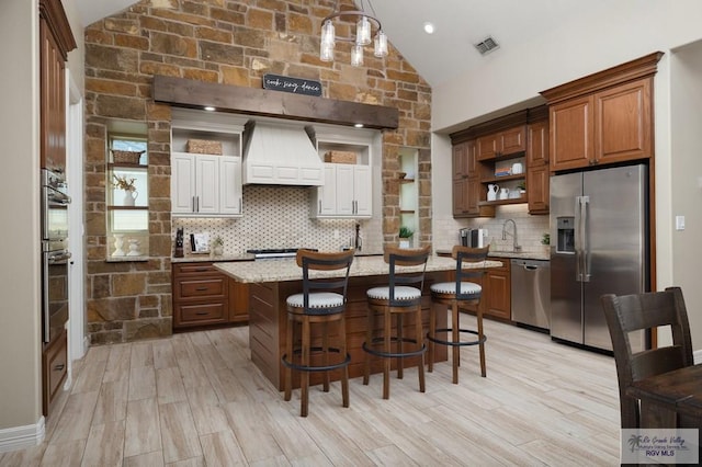 kitchen featuring custom exhaust hood, stainless steel appliances, decorative light fixtures, light hardwood / wood-style floors, and lofted ceiling