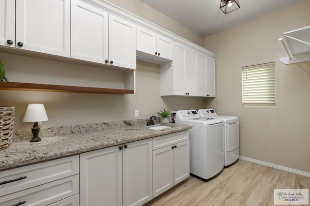 laundry room with washing machine and clothes dryer, sink, cabinets, and light hardwood / wood-style flooring