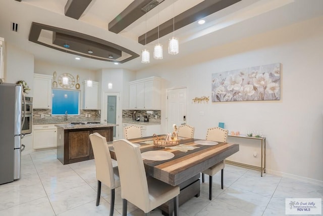 dining area featuring a raised ceiling, sink, and beam ceiling