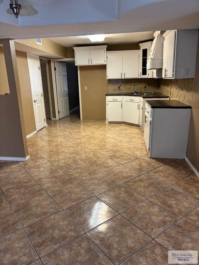 kitchen with decorative backsplash, dark tile patterned flooring, custom range hood, and white cabinets