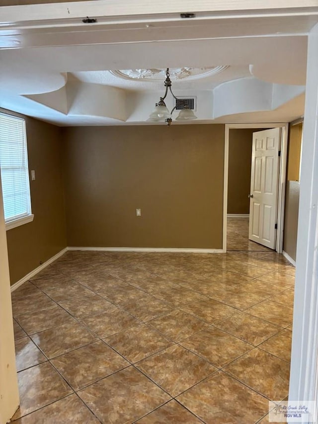 empty room with a raised ceiling, tile patterned flooring, and an inviting chandelier