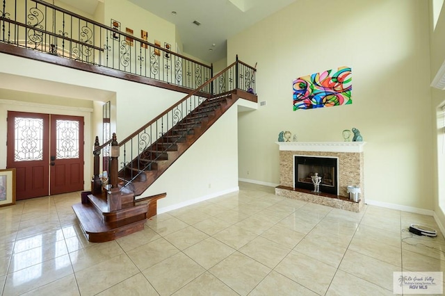 tiled entryway with french doors, a premium fireplace, and a high ceiling