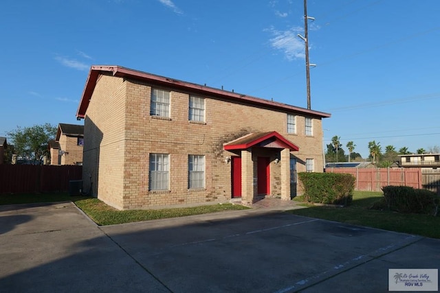 view of front of house with uncovered parking, brick siding, and fence