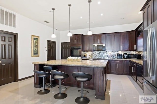 kitchen with light stone countertops, tasteful backsplash, stainless steel appliances, decorative light fixtures, and an island with sink