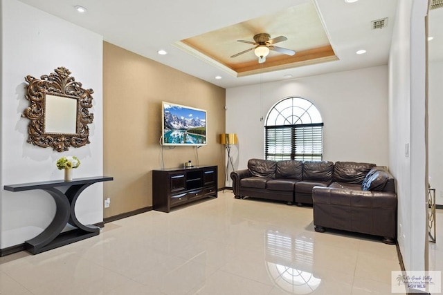 tiled living room featuring ceiling fan and a tray ceiling