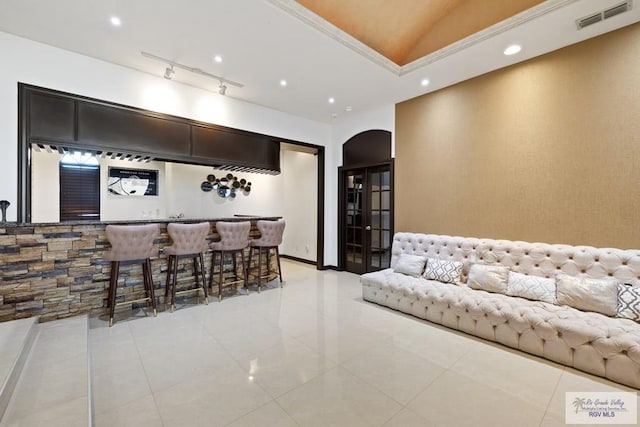 tiled living room featuring bar area, vaulted ceiling, and ornamental molding