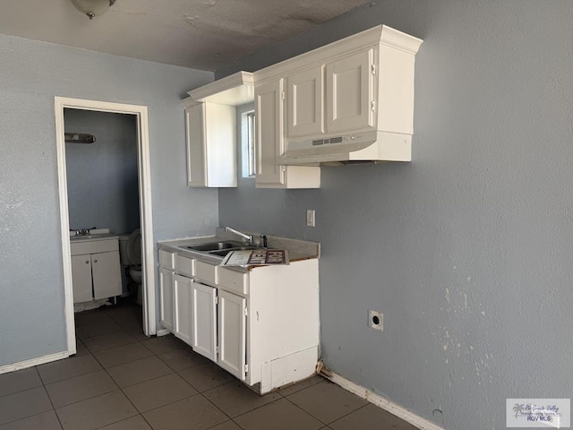 1000 Combes St, San Benito, TX 78586 - kitchen with a sink, under cabinet range hood, white cabinetry, dark tile patterned floors, and baseboards