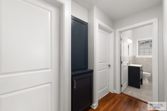 corridor with dark wood-type flooring, a sink, and tile walls