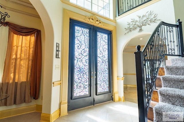 tiled foyer entrance featuring ornamental molding, a towering ceiling, and french doors