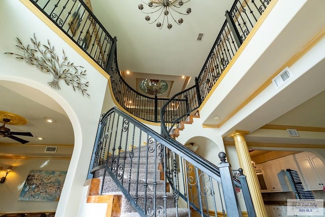 staircase with ceiling fan, a towering ceiling, ornamental molding, and decorative columns