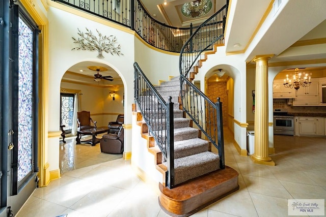 tiled entryway featuring ceiling fan with notable chandelier, decorative columns, and a high ceiling