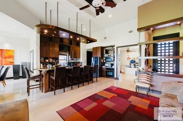 kitchen with kitchen peninsula, a kitchen breakfast bar, ceiling fan, and a high ceiling