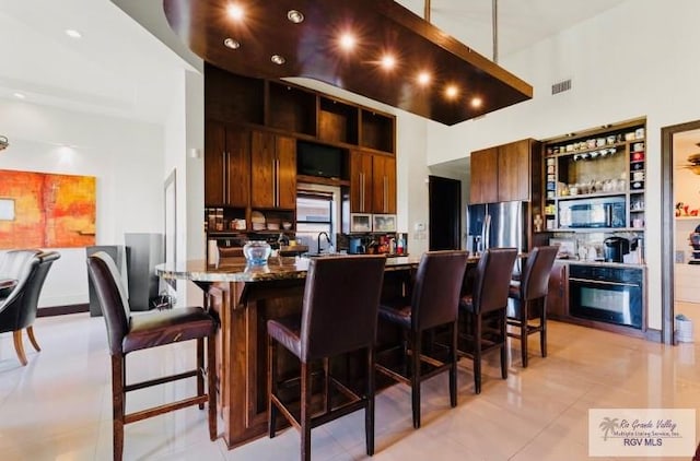 kitchen with stainless steel appliances, a high ceiling, a kitchen breakfast bar, light stone counters, and light tile patterned floors