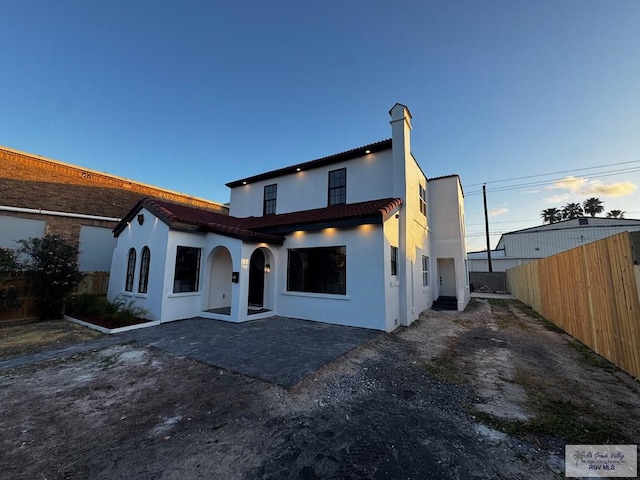 view of front of house featuring stucco siding, a tiled roof, fence, and a patio