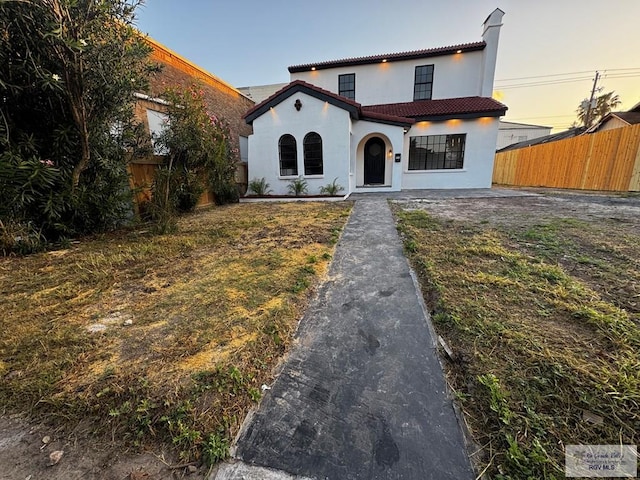 mediterranean / spanish-style home with a tile roof, fence, and stucco siding