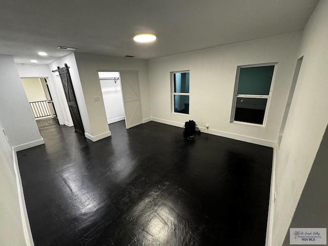 unfurnished room with a barn door, visible vents, and baseboards