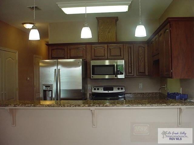 kitchen featuring kitchen peninsula, appliances with stainless steel finishes, hanging light fixtures, and dark stone countertops