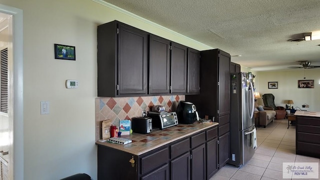 kitchen with tasteful backsplash, freestanding refrigerator, tile countertops, light tile patterned floors, and ceiling fan