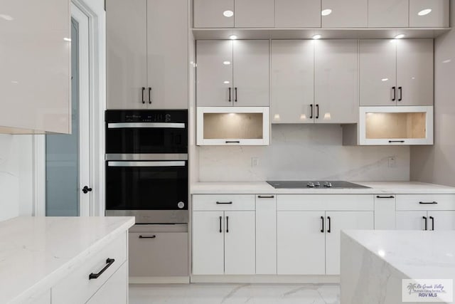 kitchen featuring black electric stovetop, stainless steel double oven, white cabinetry, and light stone counters