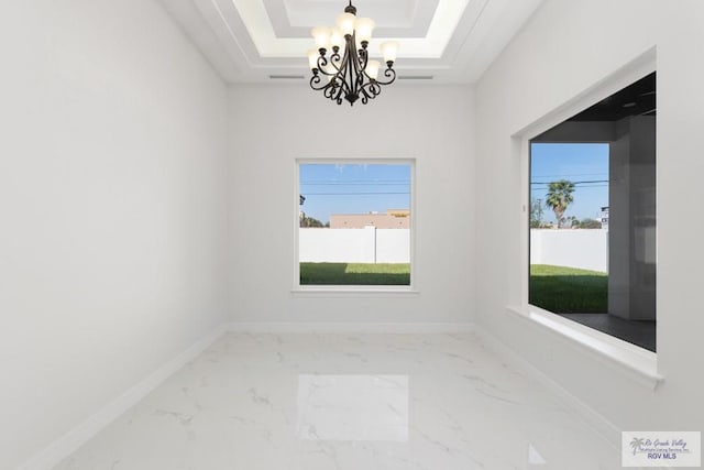 spare room with a raised ceiling and an inviting chandelier