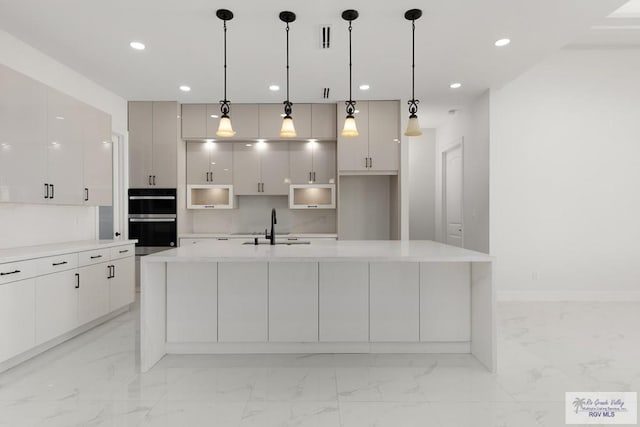 kitchen featuring sink, an island with sink, stainless steel double oven, and decorative light fixtures