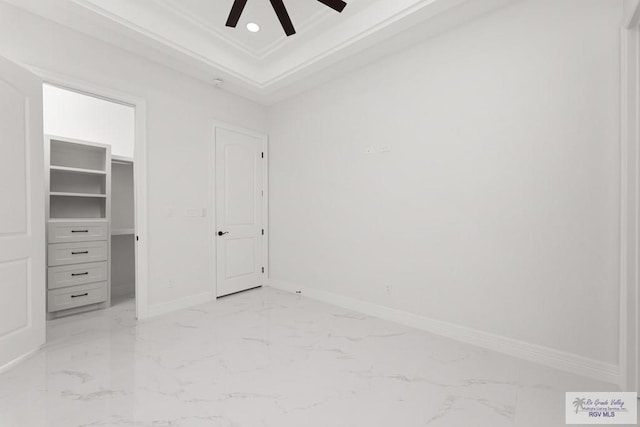 unfurnished bedroom featuring ceiling fan, a raised ceiling, crown molding, a walk in closet, and a closet