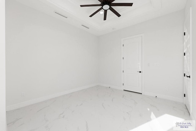 empty room with ceiling fan and a raised ceiling