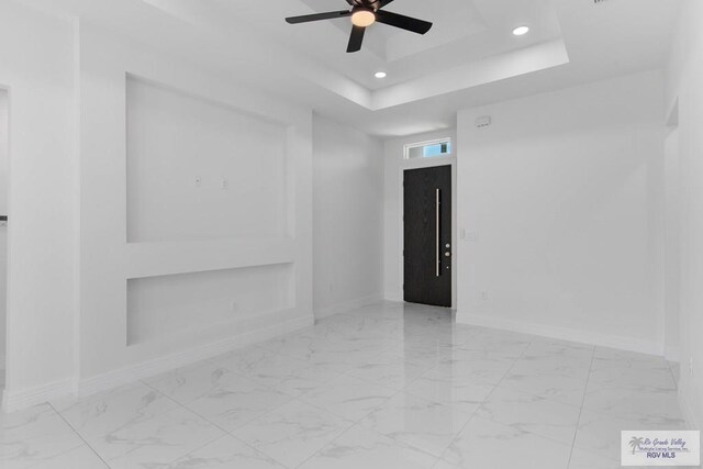 empty room with a tray ceiling, elevator, and ceiling fan