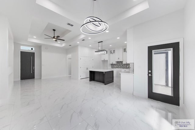 unfurnished living room with ceiling fan with notable chandelier and a tray ceiling