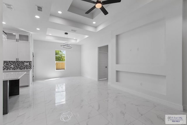 unfurnished living room with a raised ceiling and ceiling fan