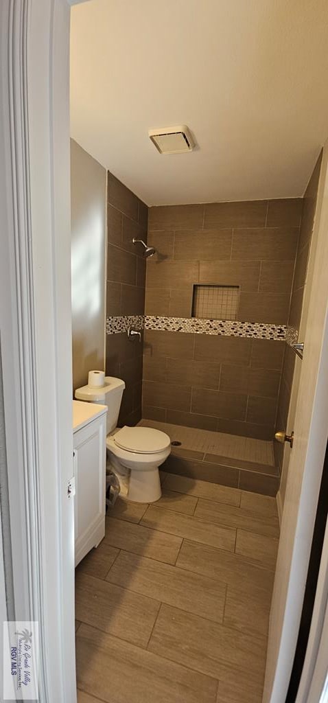 bathroom featuring vanity, tiled shower, and toilet