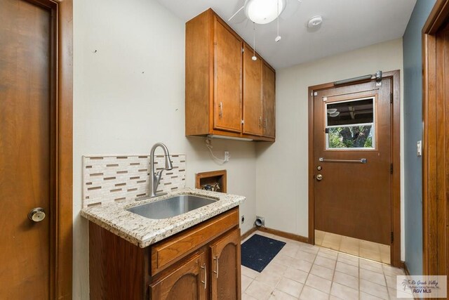 kitchen with decorative backsplash, light tile patterned floors, light stone counters, and sink