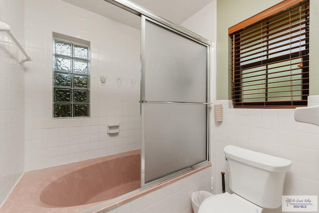 bathroom with combined bath / shower with glass door, toilet, and tile walls