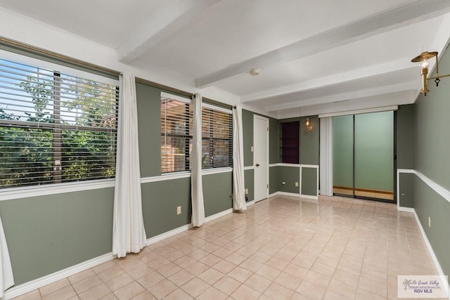 empty room with beamed ceiling and light tile patterned flooring